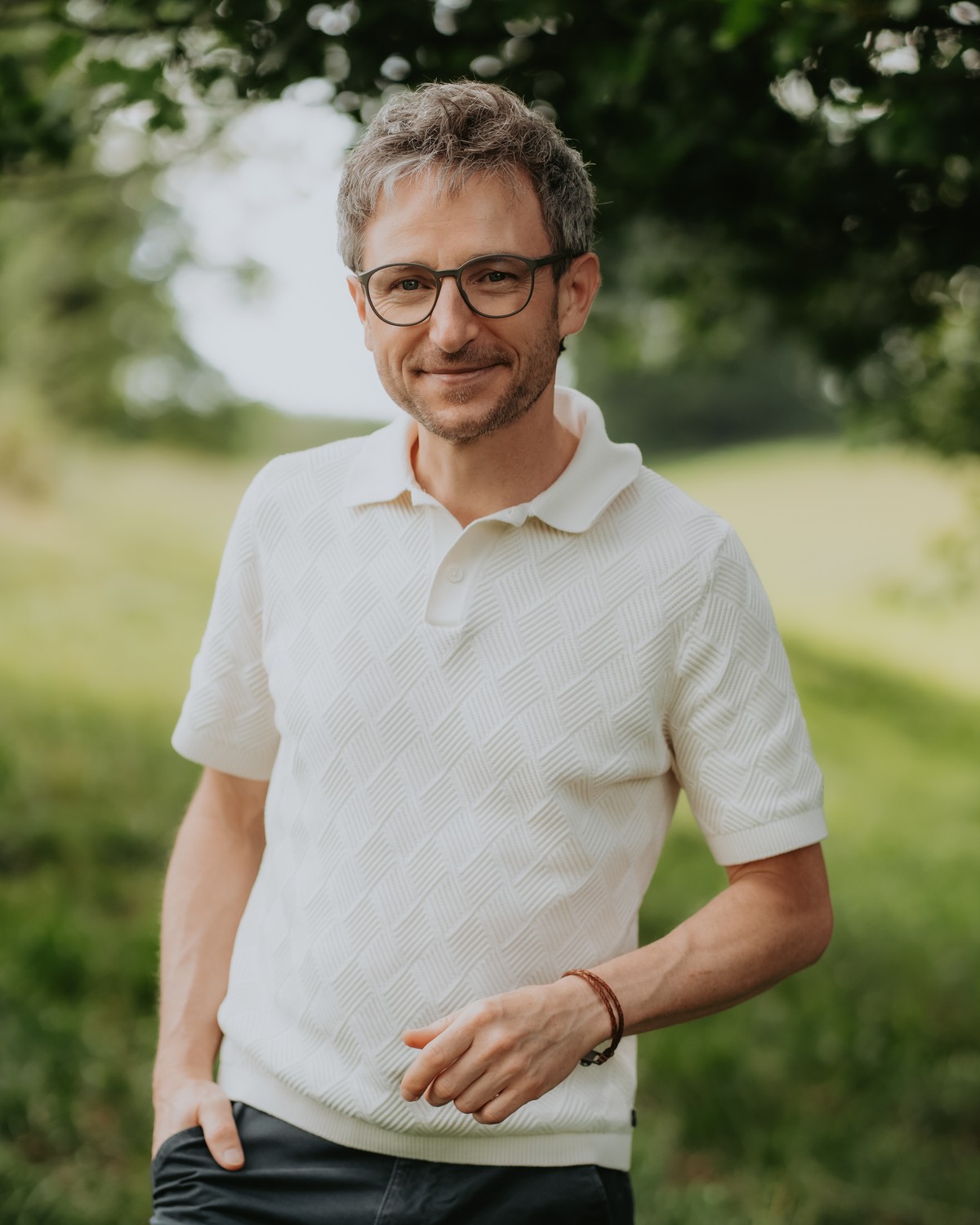 Tobias Weise lächelt im Gegenlicht einer Sommerwiese in die Kamera, Kopf und Schultern nah.