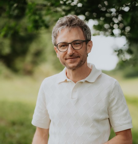 Tobias Weise steht auf einer sommerlichen Wiese und lächelt in die Kamera.