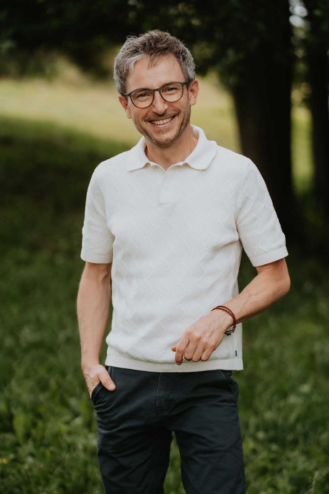 Porträt von Tobias Weise, Der Energieweise, in der Natur: freundlich lächelnd auf einer Sommerwiese vor Bäumen